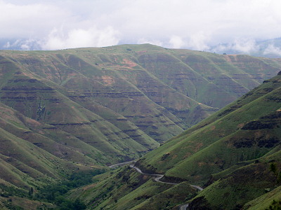 [The canyon walls are deep and covered in low-to-the-ground vegetation. There is scoring at many levels as if there once was water at each of the levels in the canyon.]